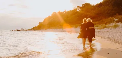 To personer går langs stranden ved solnedgang