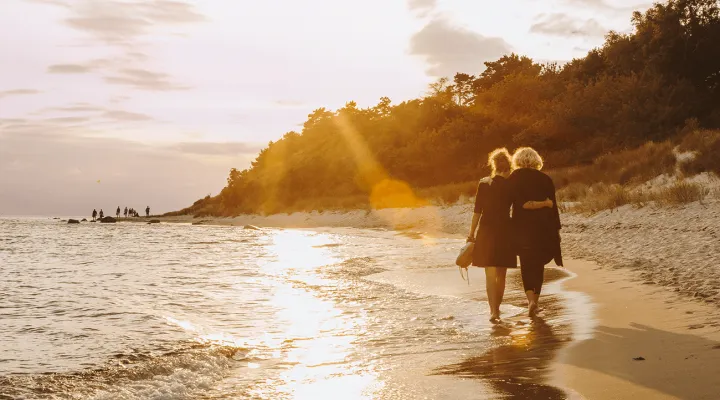 Par går ved siden af hinanden i vandkanten på stranden ved solnedgang