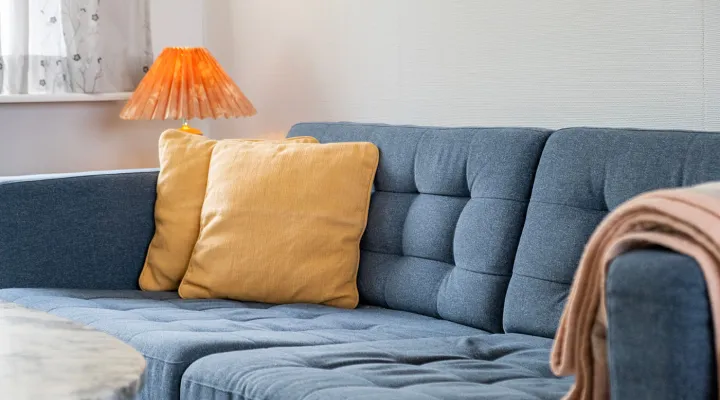 Sofa med gule pyntepuder og tæppe i ferielejlighed Gnisten