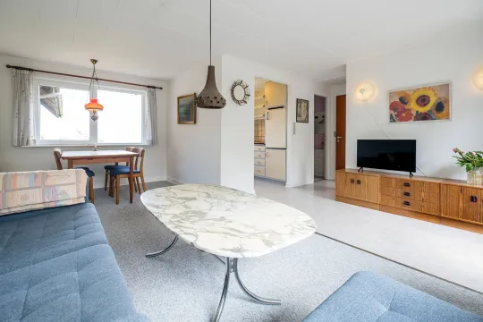 Stue med spisebord, TV og åben forbindelse til køkken i ferielejlighed Gnisten