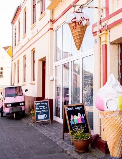 Gudhjem Is' facade med skilte og lille, lyserød scooter
